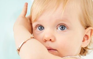 Grey eyed toddler holding their arm up and wearing a rose gold baby bangle from Little Star